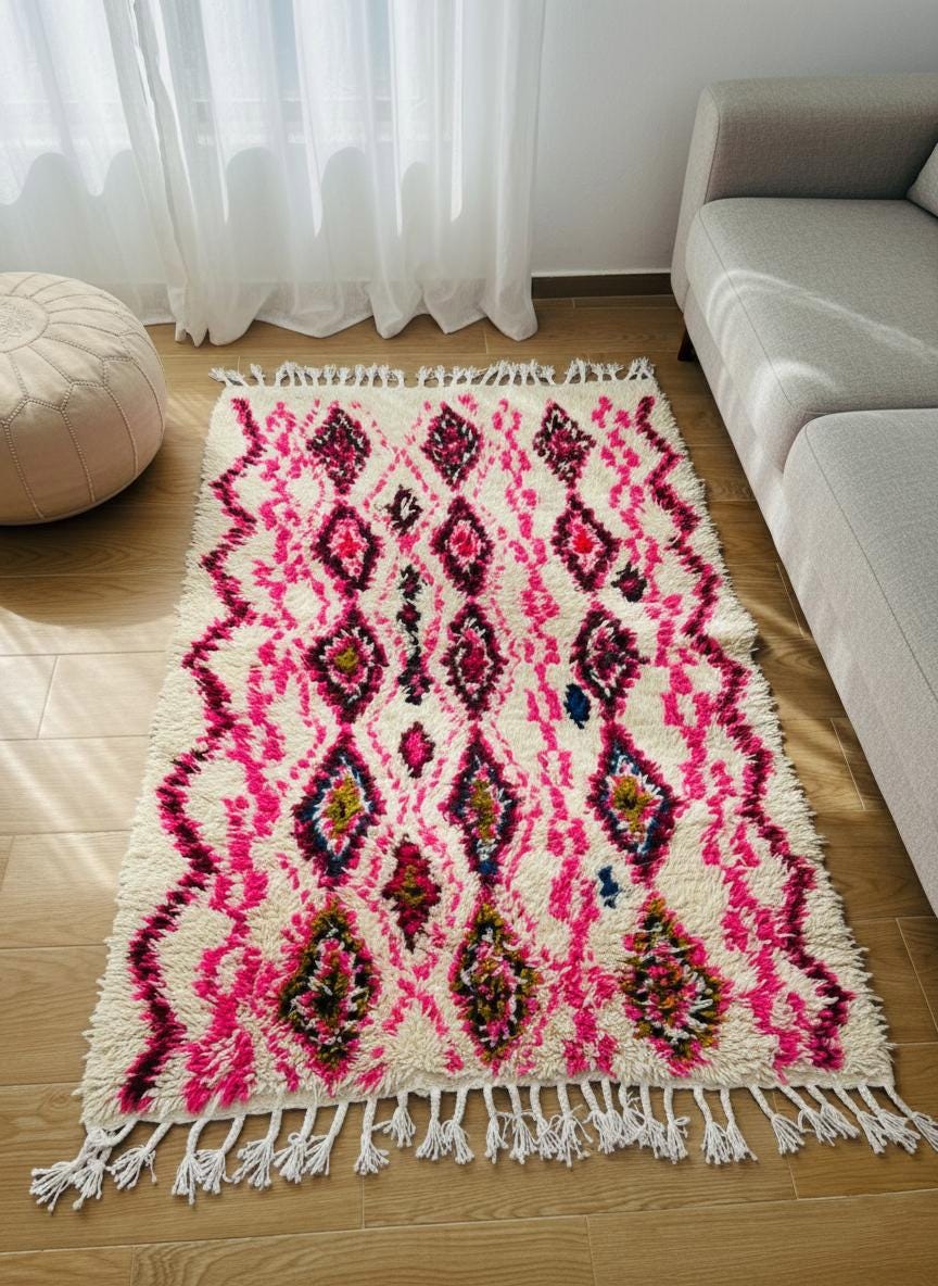 Small beige and pink Moroccan rug with tassels on wooden floor