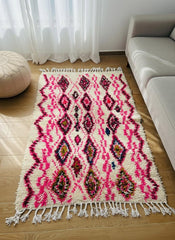 Small beige and pink Moroccan rug with tassels on wooden floor