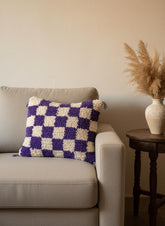 Moroccan tufted wool pillow in purple and cream on a beige sofa.
