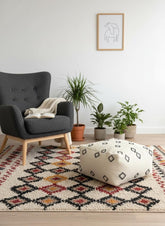 Ivory Moroccan wool pouf with black square pattern on colorful Berber rug.