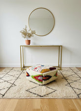 Square tribal wool pouf under console table with round mirror.
