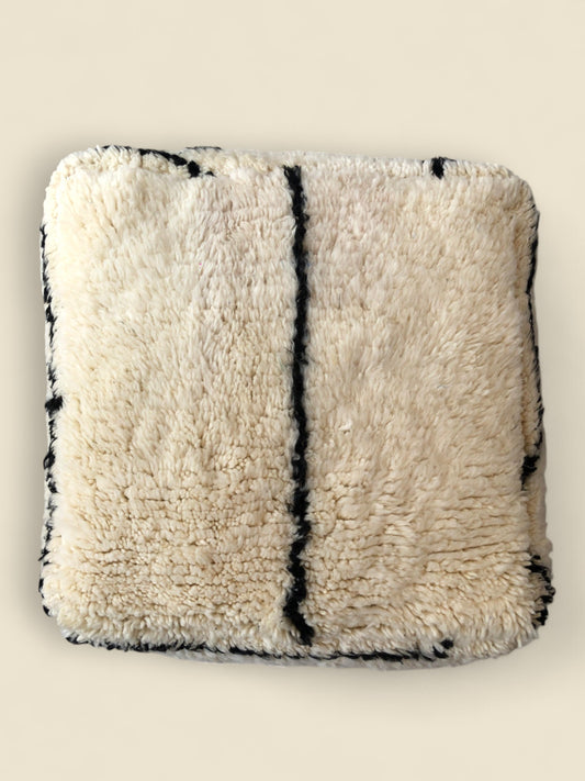 Handwoven Moroccan pouffe in natural wool with black line detail – top view.