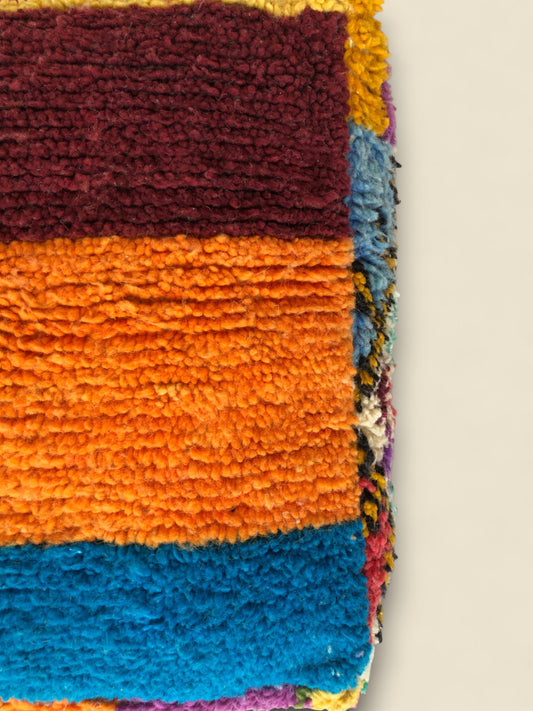 Detailed close-up of pouffe texture featuring thick orange and blue wool