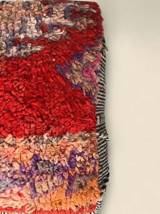 Top corner of the Tislit pouffe with rich red center and abstract blend of earthy wool colors.