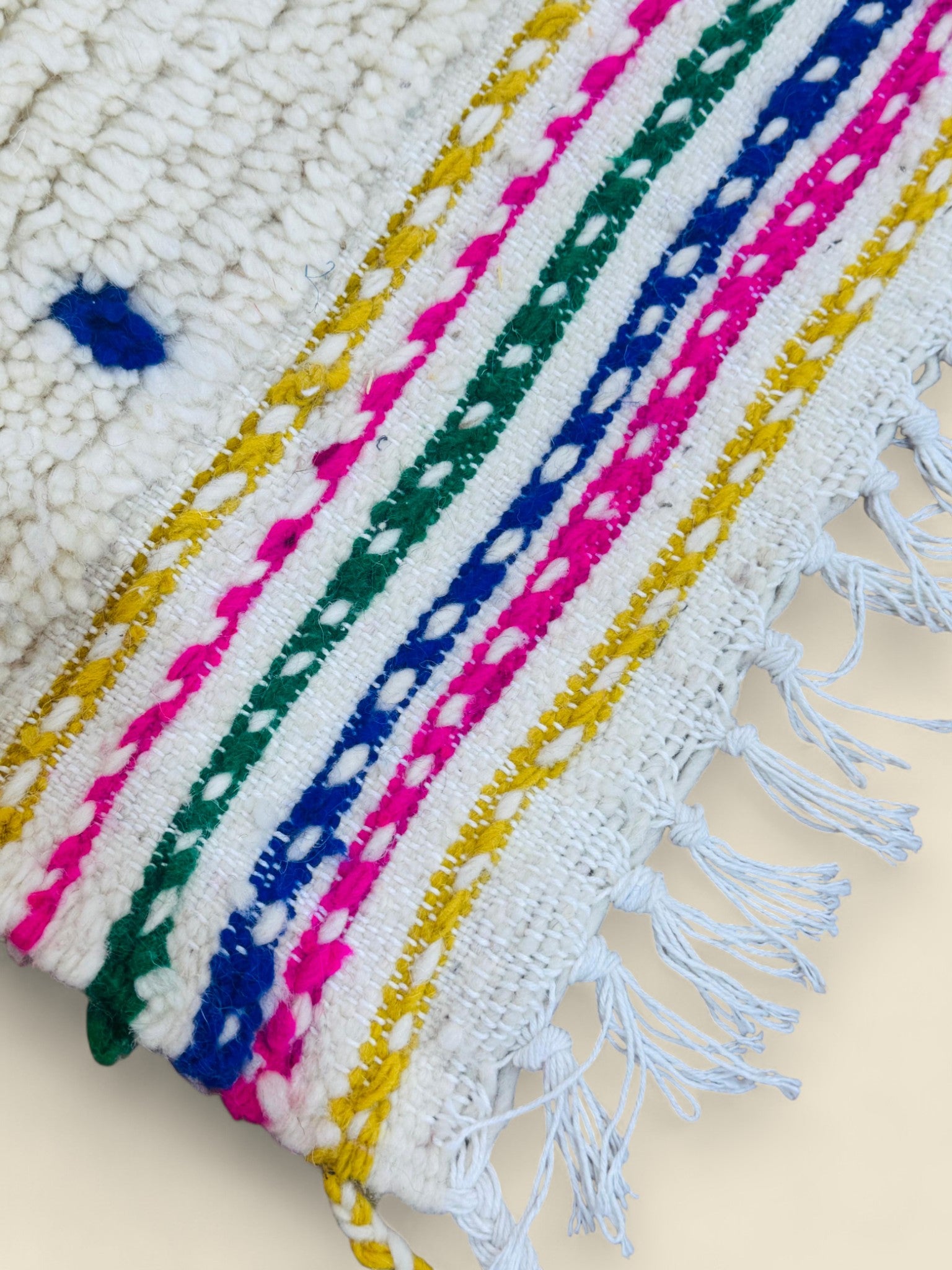 Close-up of woven rug border with pink, green, yellow, and blue stripes.