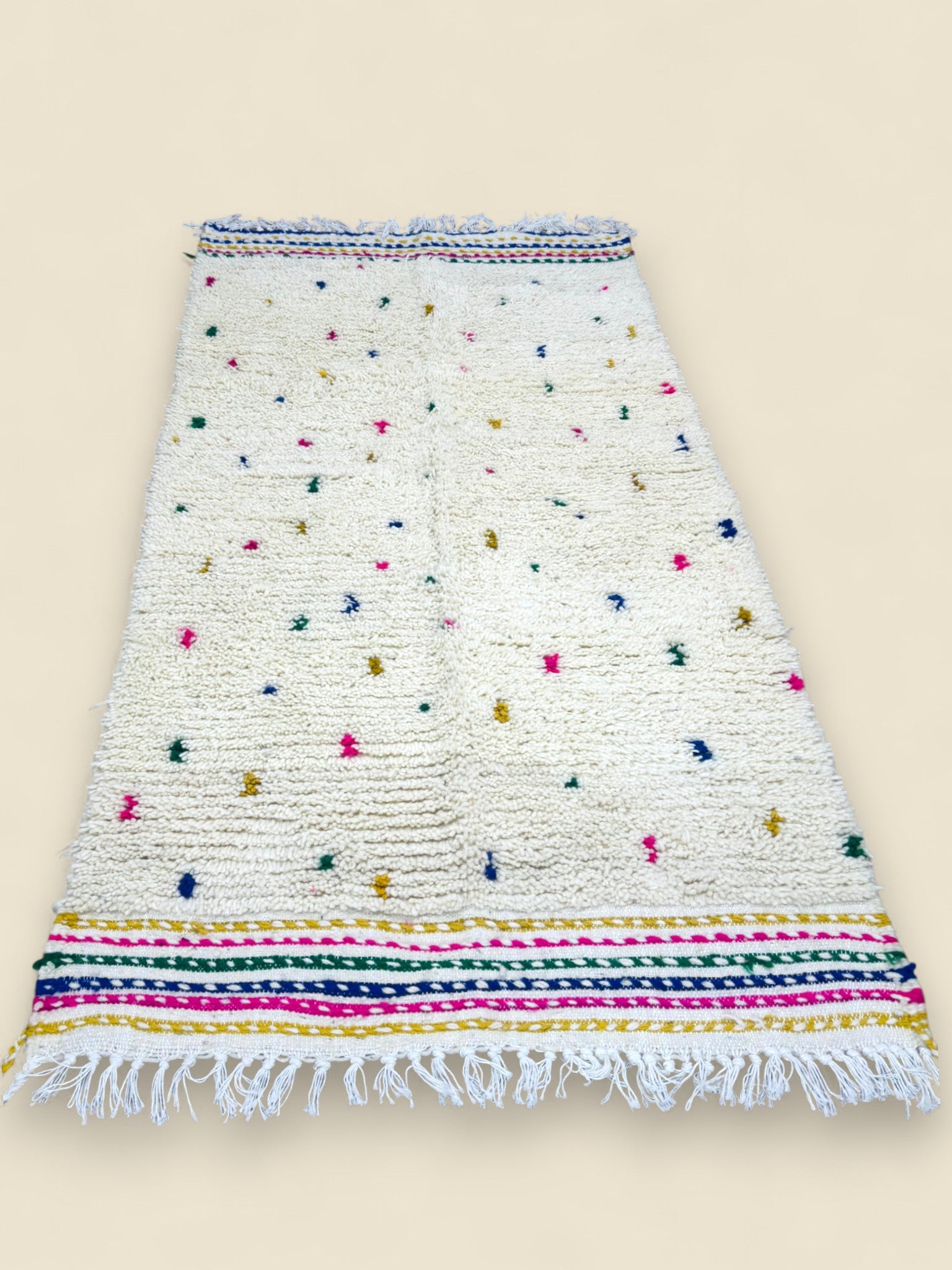 White Moroccan rug with colorful dot pattern and fringed edges.