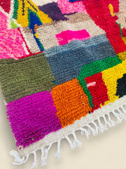 Corner view of Tawenza Berber rug with purple, orange, and green tones.