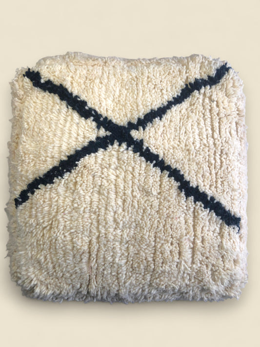 Cream wool Moroccan pouffe with bold black cross design, handwoven in traditional Berber style.