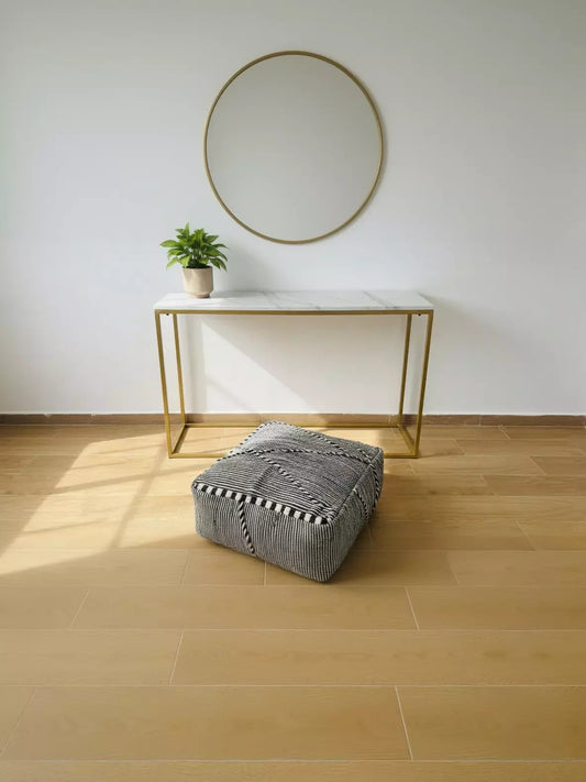 Handwoven Tamazirt pouf on wooden floor near console table.