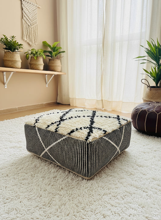 Berber wool pouf placed in a bright bohemian room with plants.