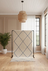 Beige and blue diamond patterned rug on a wooden floor with a wicker lamp and plant in the background.