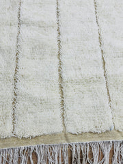 Close-up of Tazgart cream wool rug with raised linear texture and fringe edges.