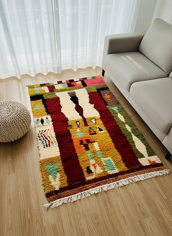 Small Moroccan wool rug with colorful abstract design placed beside a sofa in a sunlit corner.