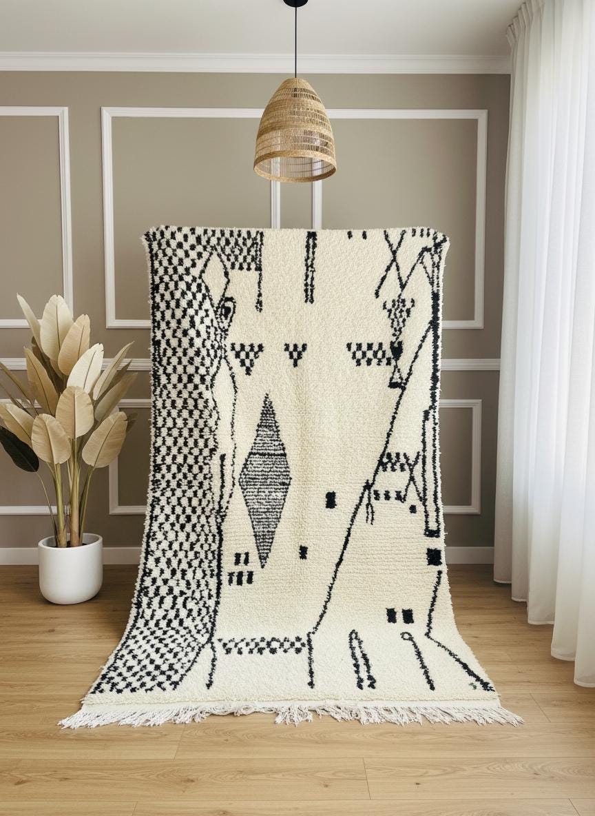 Handmade ivory Berber rug with black tribal motifs displayed vertically in a minimalist interior with wood floor and pendant light