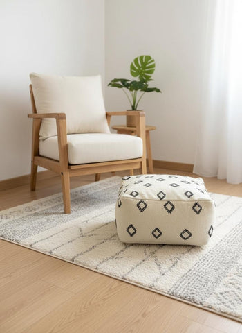 Neutral square Berber pouf styled beside modern armchair and plants.