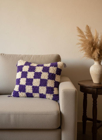 Moroccan tufted wool pillow in purple and cream on a beige sofa.