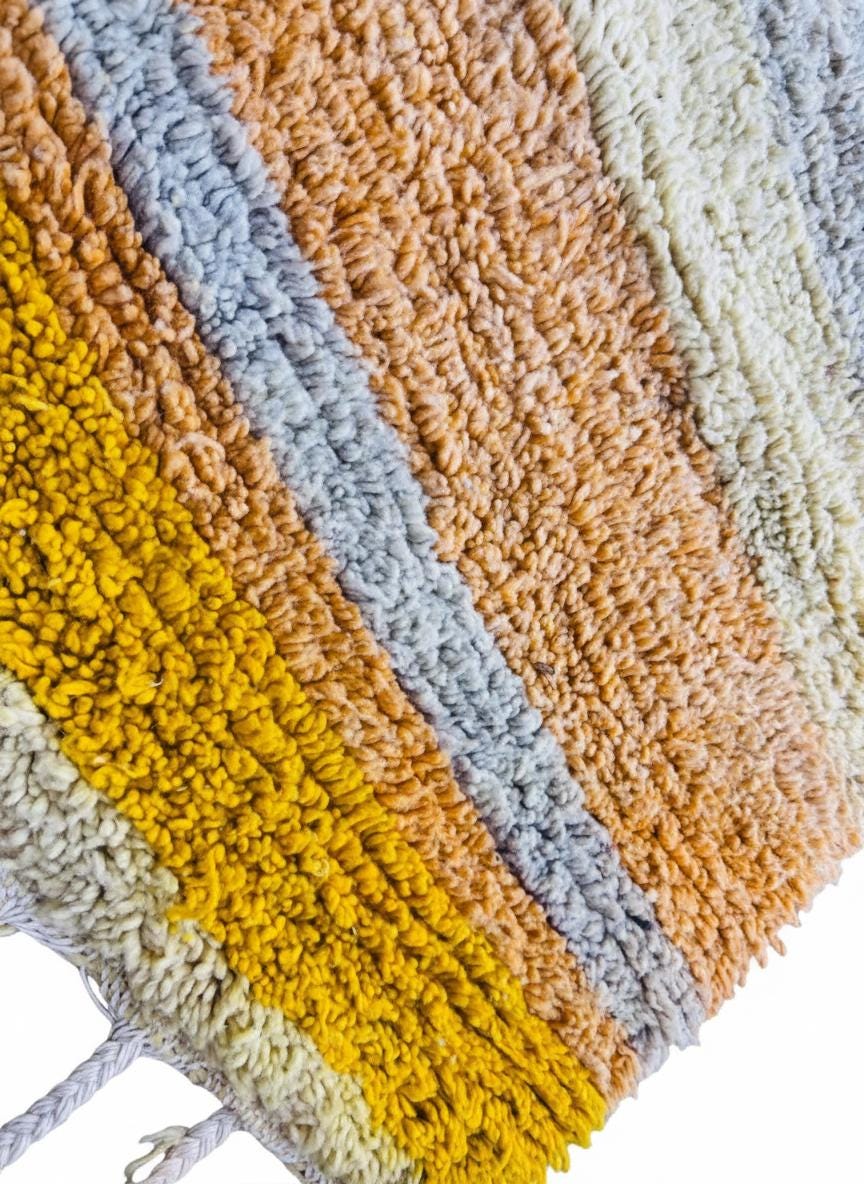 Close-up of handmade Moroccan yellow Berber wool rug with geometric pattern and fringe.