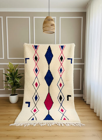 Handmade Moroccan Berber rug displayed vertically with blue and pink diamond pattern on a cream wool base.
