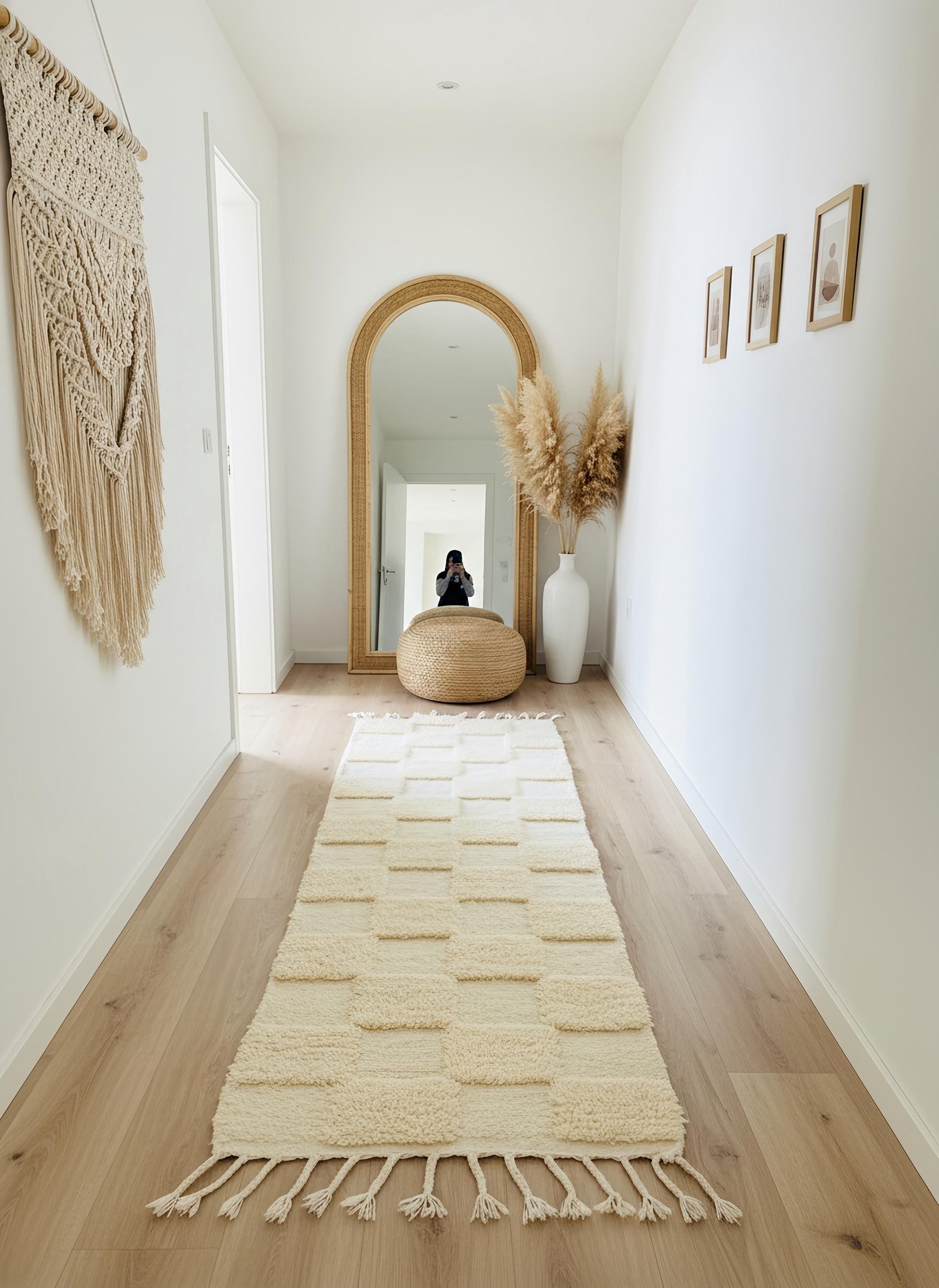Neutral wool runner rug with soft textured squares styled in a minimalist hallway with arched floor mirror and pampas grass.