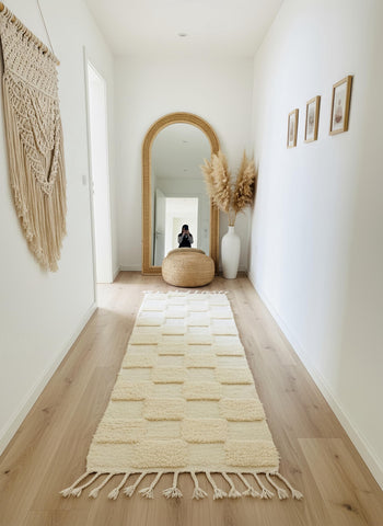 Neutral wool runner rug with soft textured squares styled in a minimalist hallway with arched floor mirror and pampas grass.