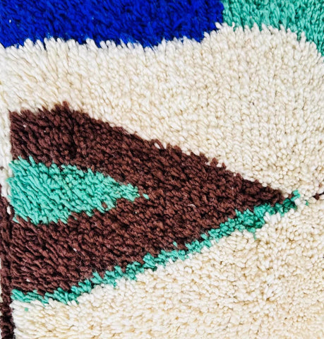 Close-up detail of a handmade Moroccan wool pouf featuring a tufted geometric pattern in brown and mint green on an ivory wool background.