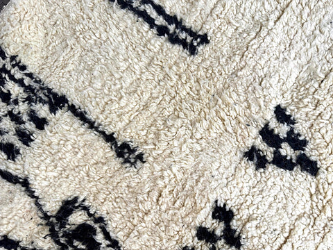 Close-up of Moroccan wool rug showing thick plush texture with black geometric details on cream background