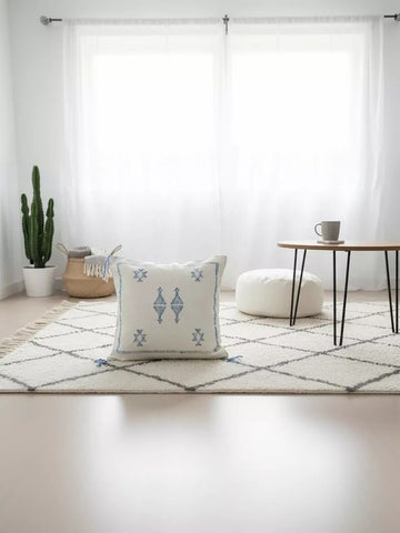 Handwoven Moroccan Tilya Berber pillow in cream and blue with tribal pattern on rug