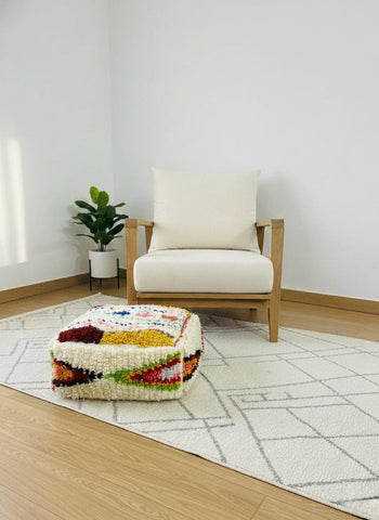 Handmade multicolor Moroccan pouf styled beside wooden armchair.