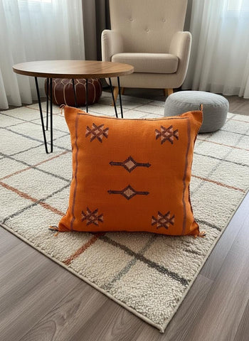 Orange Moroccan Berber pillow with tribal embroidery on living room rug.
