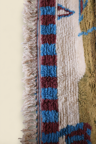 Side view of Moroccan rug with cream fringes and blue, burgundy, and cream geometric border pattern