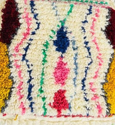 Close-up of cream wool pouf with colorful Berber tribal pattern.