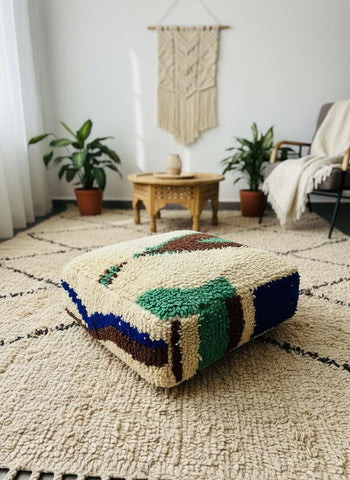 Handcrafted Berber floor pouf with colorful geometric design styled on a textured cream rug in a cozy bohemian interior.