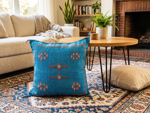Handwoven blue Sabra pillow displayed on a patterned rug in a cozy living room.