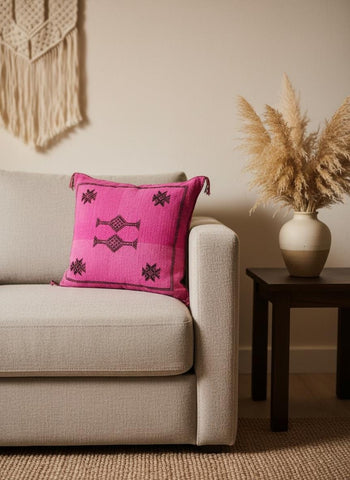 Moroccan cactus silk cushion in bright pink with tribal embroidery styled on a textured rug in a modern living space.