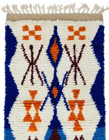 Handwoven Moroccan runner rug featuring bold blue waves and orange tribal motifs on an ivory base with tasseled fringe.