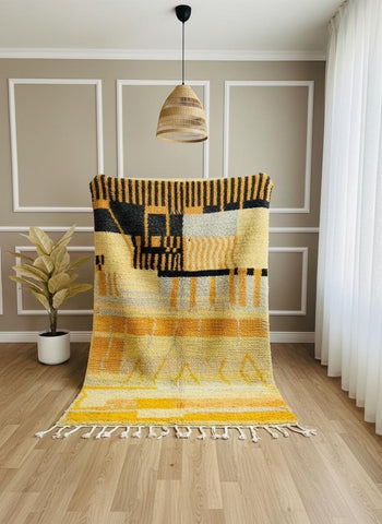 Full view of handmade Moroccan yellow rug with fringe against neutral wall.