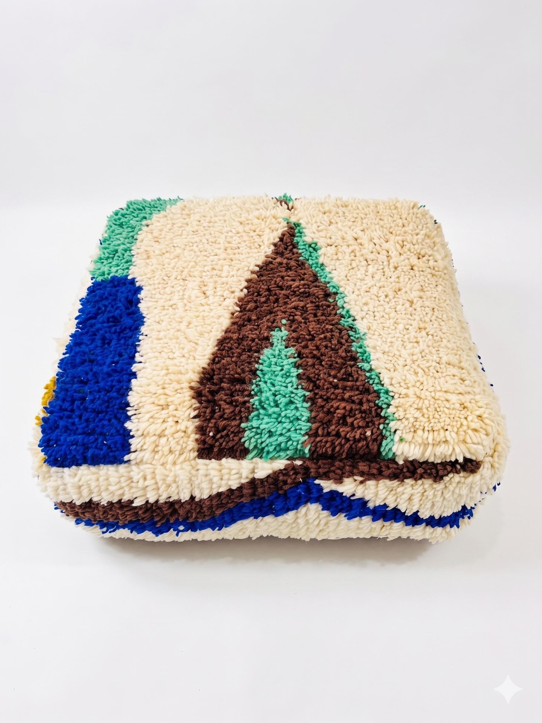 Square Moroccan wool floor pouf featuring tufted blue, green, and brown geometric motifs on an ivory background.