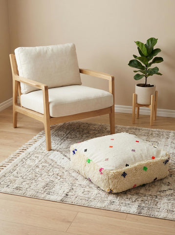 Moroccan square pouf near wooden chair and plant in minimalist interior