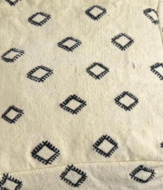 Close-up of ivory wool pouf fabric with small black geometric motifs.