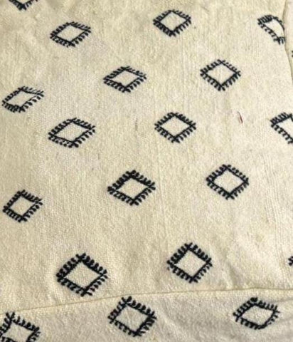 Close-up of ivory wool pouf fabric with small black geometric motifs.