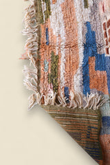Folded corner of the rug showing backside weave in olive and orange