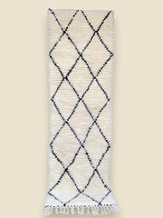 Handwoven Aicha Moroccan rug with black diamond pattern on ivory wool, finished with white fringes.