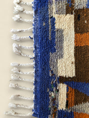 Side view of Amayas rug showcasing blue border with braided white fringes and textured wool weave.