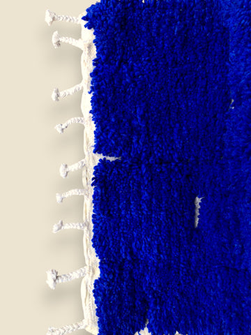 Blue textured rug with white fringe on a beige background