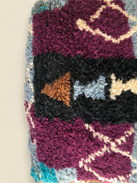 Detail of Moroccan wool pouffe featuring plum and rust-toned patterns