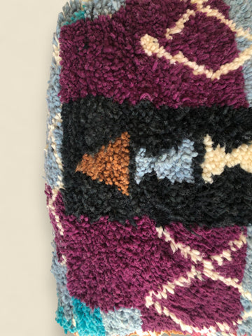 Detail of Moroccan wool pouffe featuring plum and rust-toned patterns