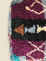 Detail of Moroccan wool pouffe featuring plum and rust-toned patterns