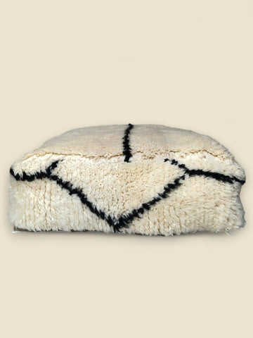 Side view of Moroccan wool pouffe with diagonal black lines and plush shape.