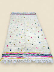 White Moroccan rug with colorful dot pattern and fringed edges.