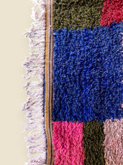 Tassadit rug corner with blue, pink, and green blocks and white fringe